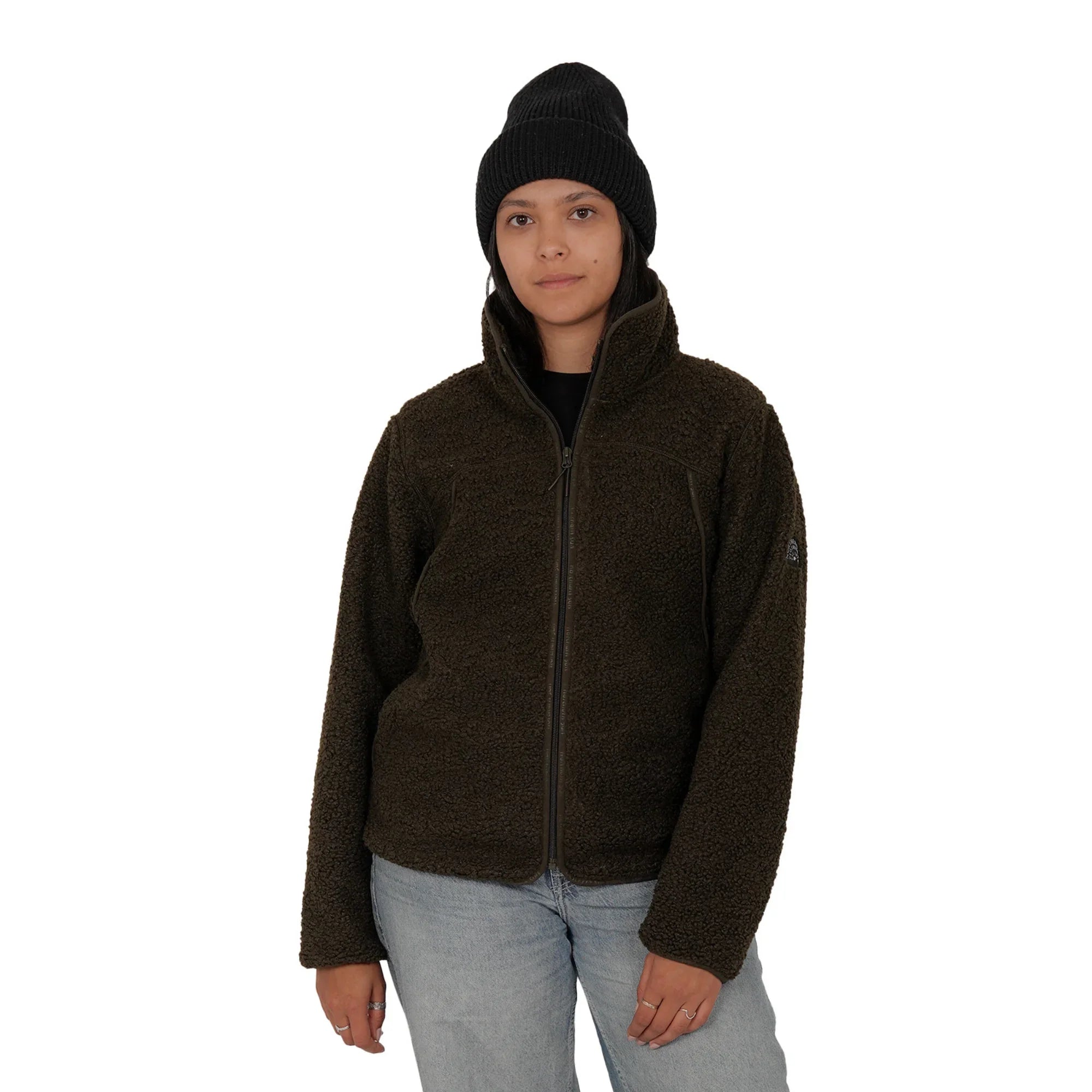 Woman wearing green teddy fleece jacket, blue jeans, and black beanie on white background