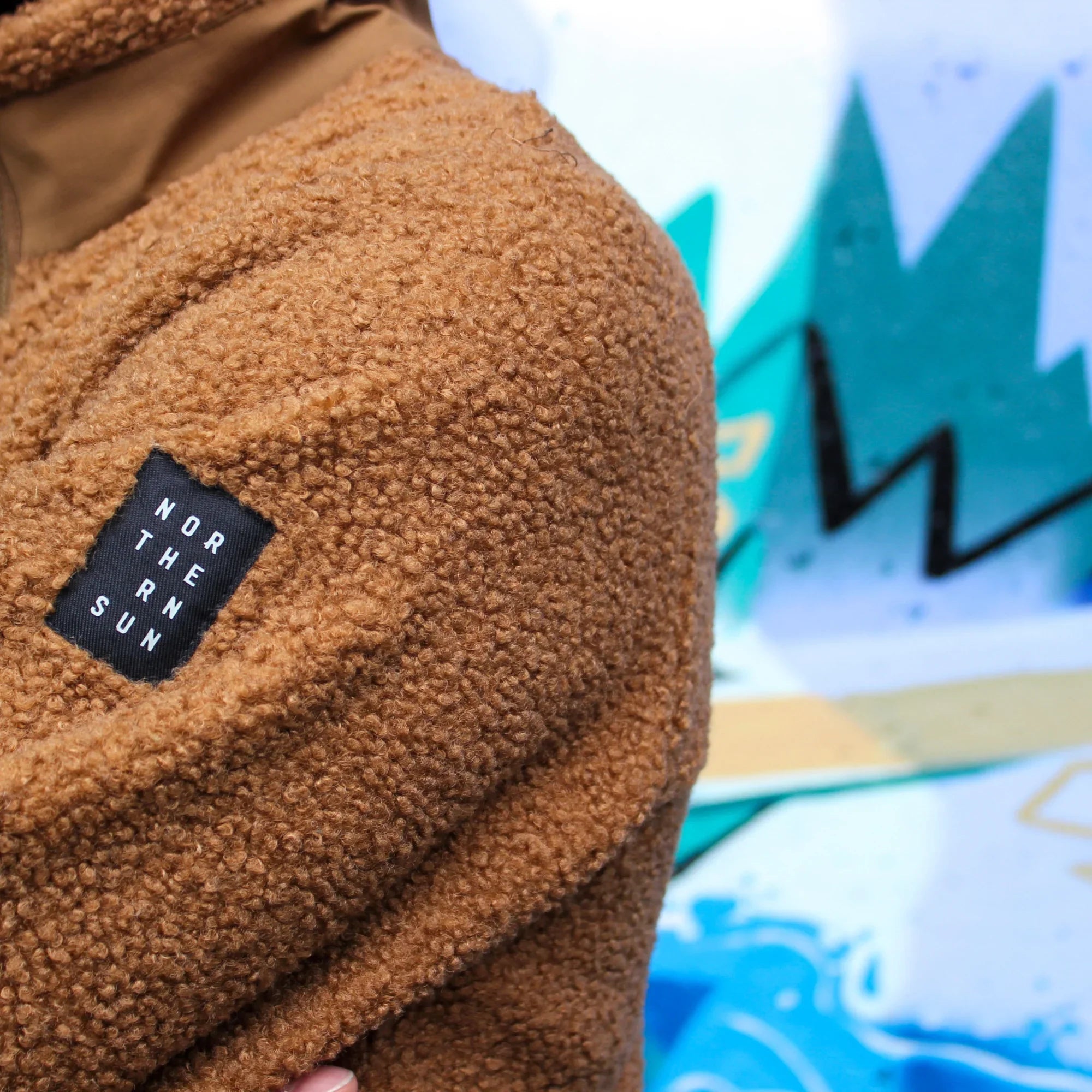 Brown teddy fleece jacket with Northern Sun logo patch, graffiti background