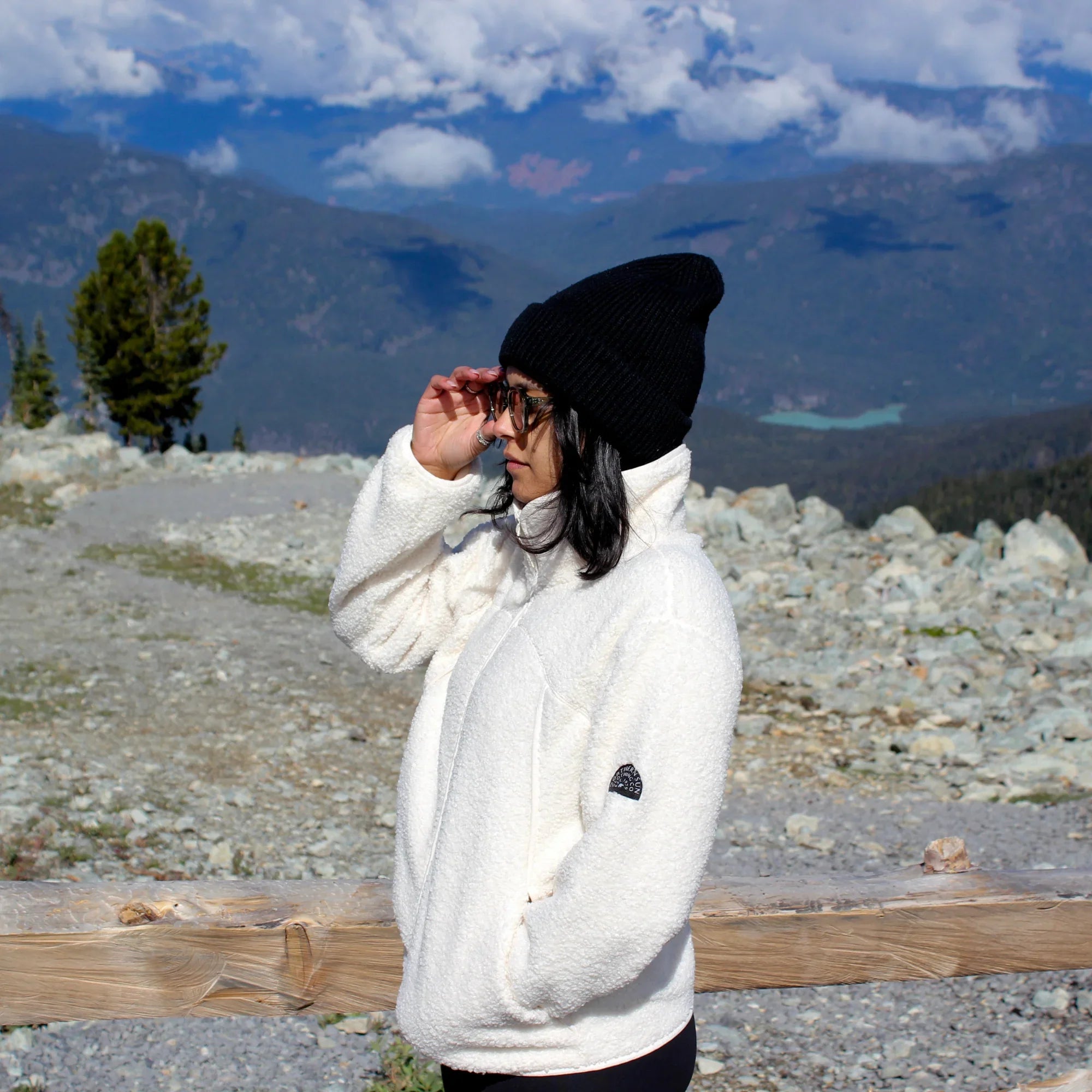 Woman in white teddy fleece jacket and black beanie on rocky mountainside with scenic view