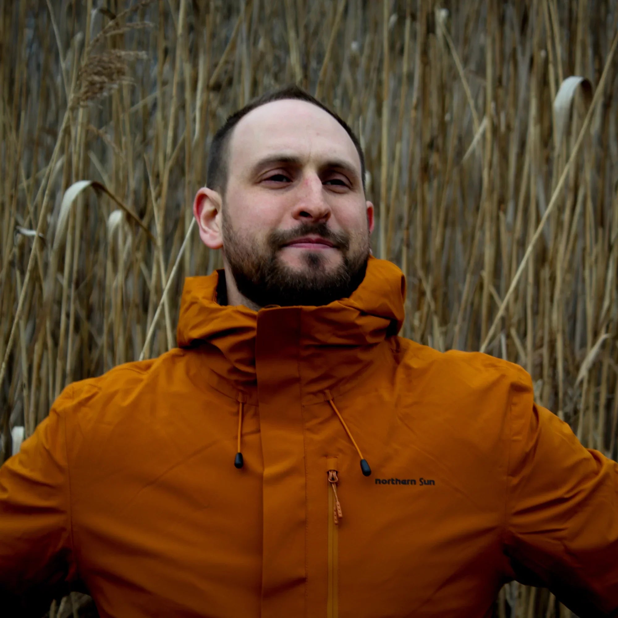 Man wearing orange Northern Sun 3-in-1 men's fall waterproof jacket outdoors in tall grass