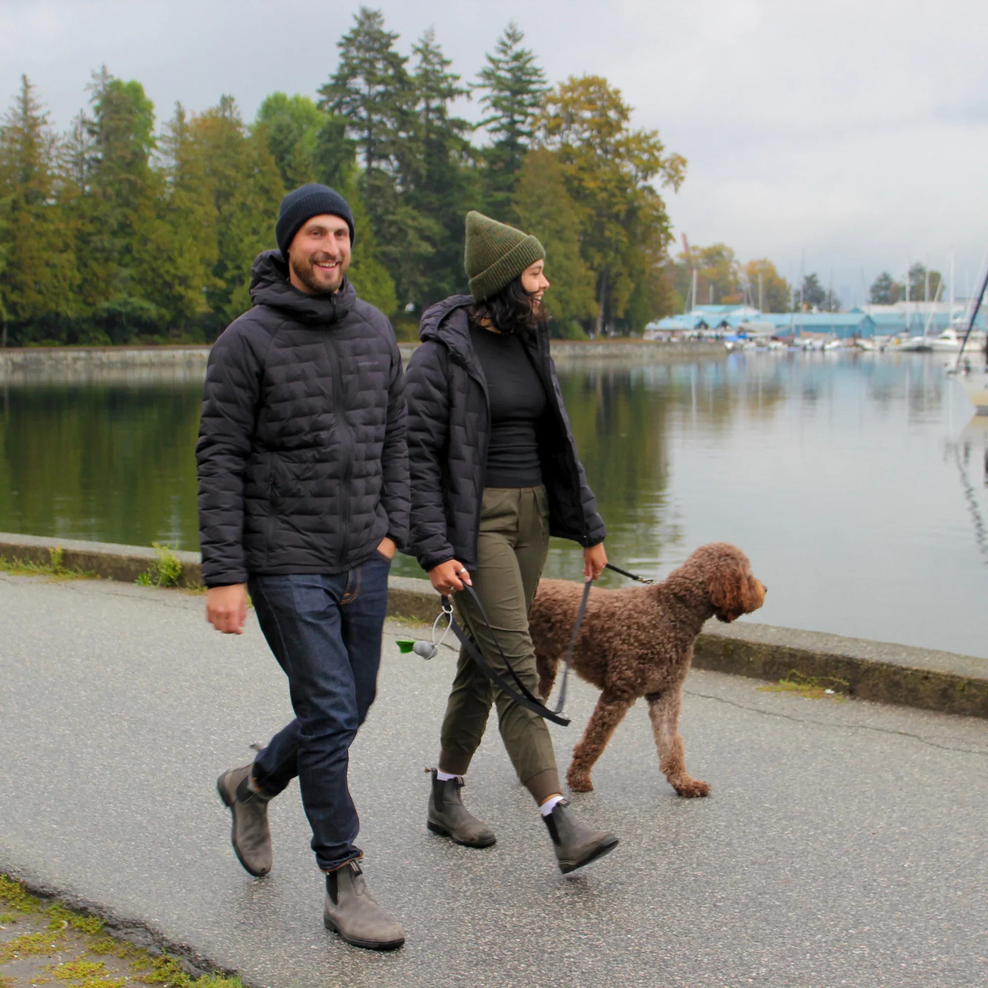 Couple wearing Dawson down jackets walking dog by city waterfront in fall