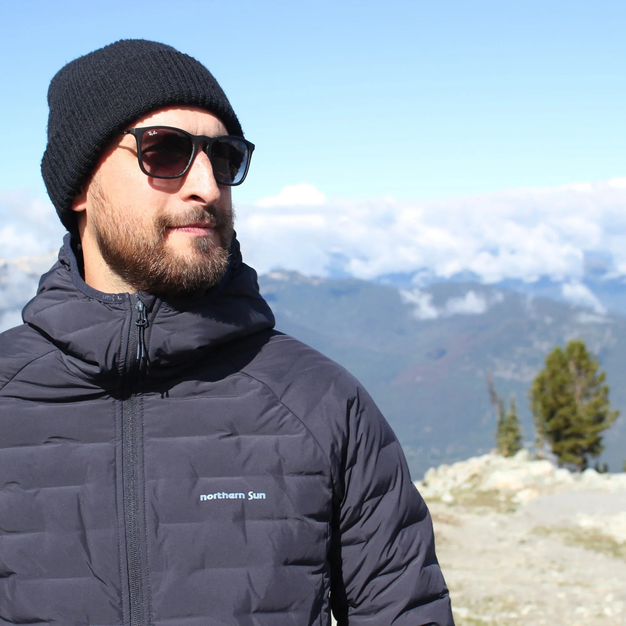 Man wearing navy Northern Sun Dawson Down waterproof jacket and beanie in mountain landscape