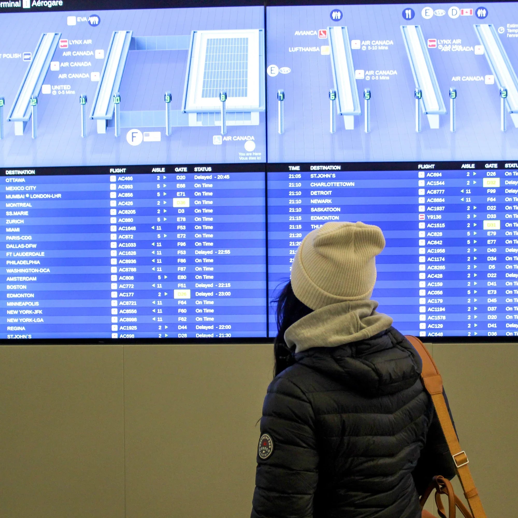 Woman in packable lightweight down jacket and beanie reading Canadian airport flight board