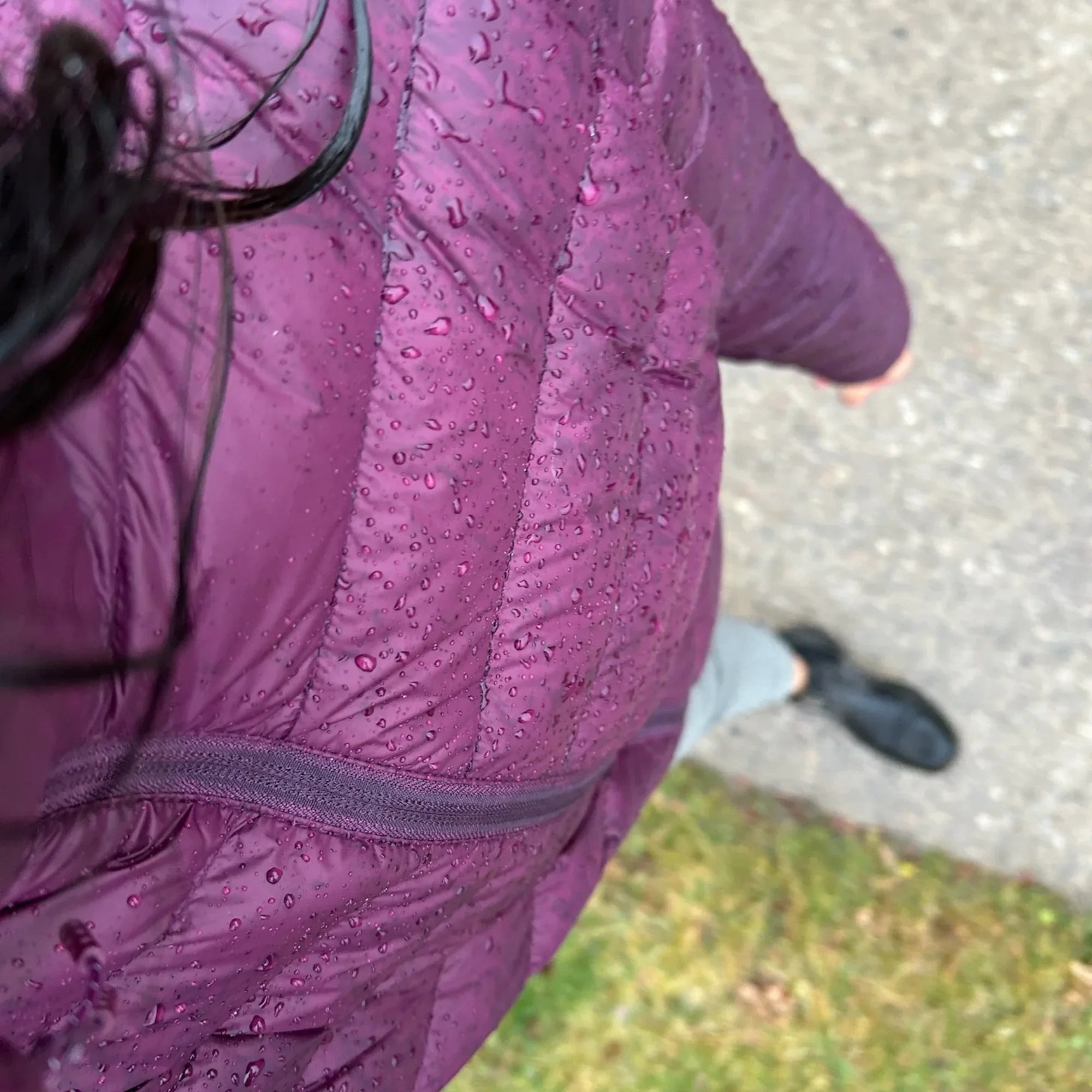 Woman in purple packable lightweight down jacket with water droplets outdoors on pavement