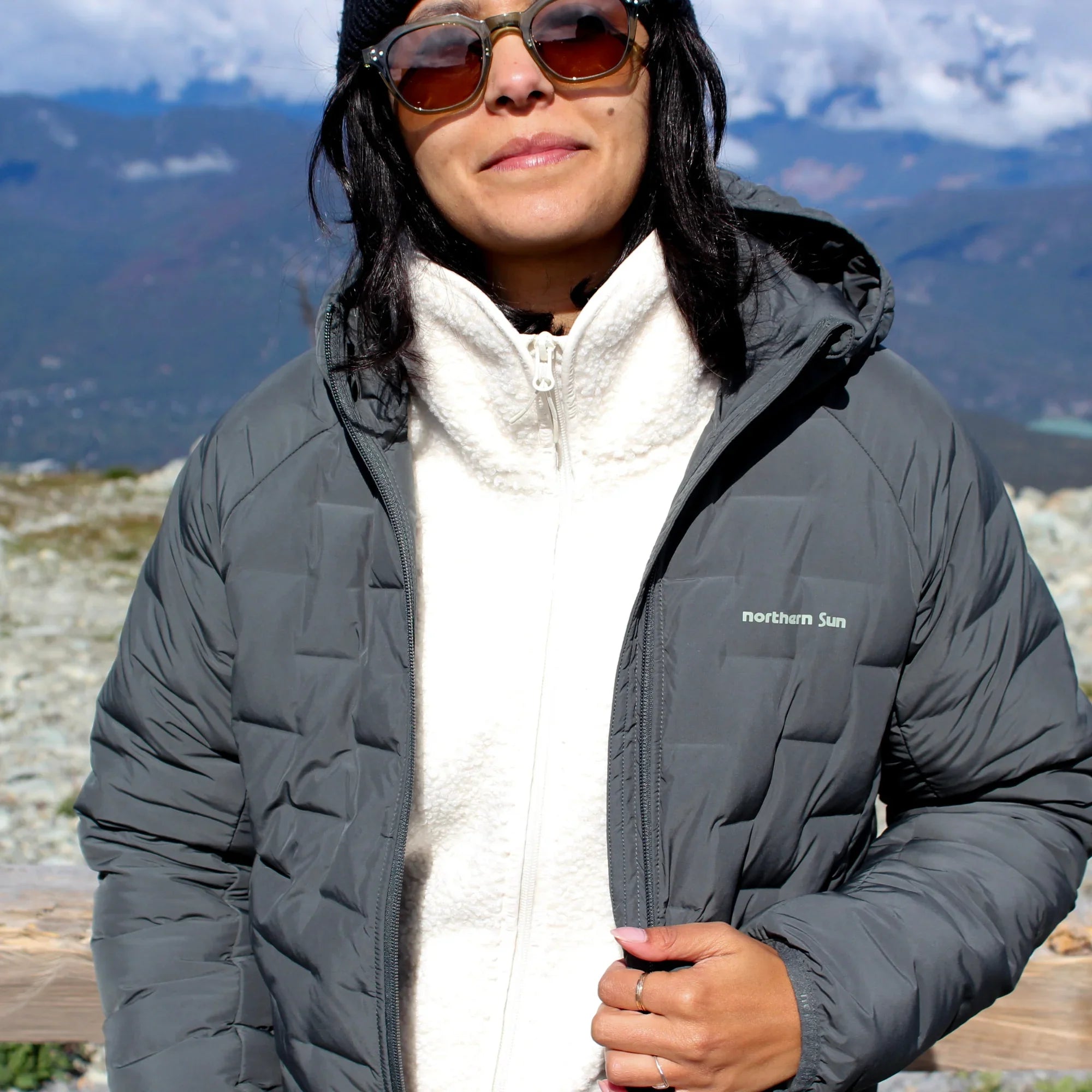 Woman wearing Northern Sun grey puffer jacket and white fleece outdoors in mountains
