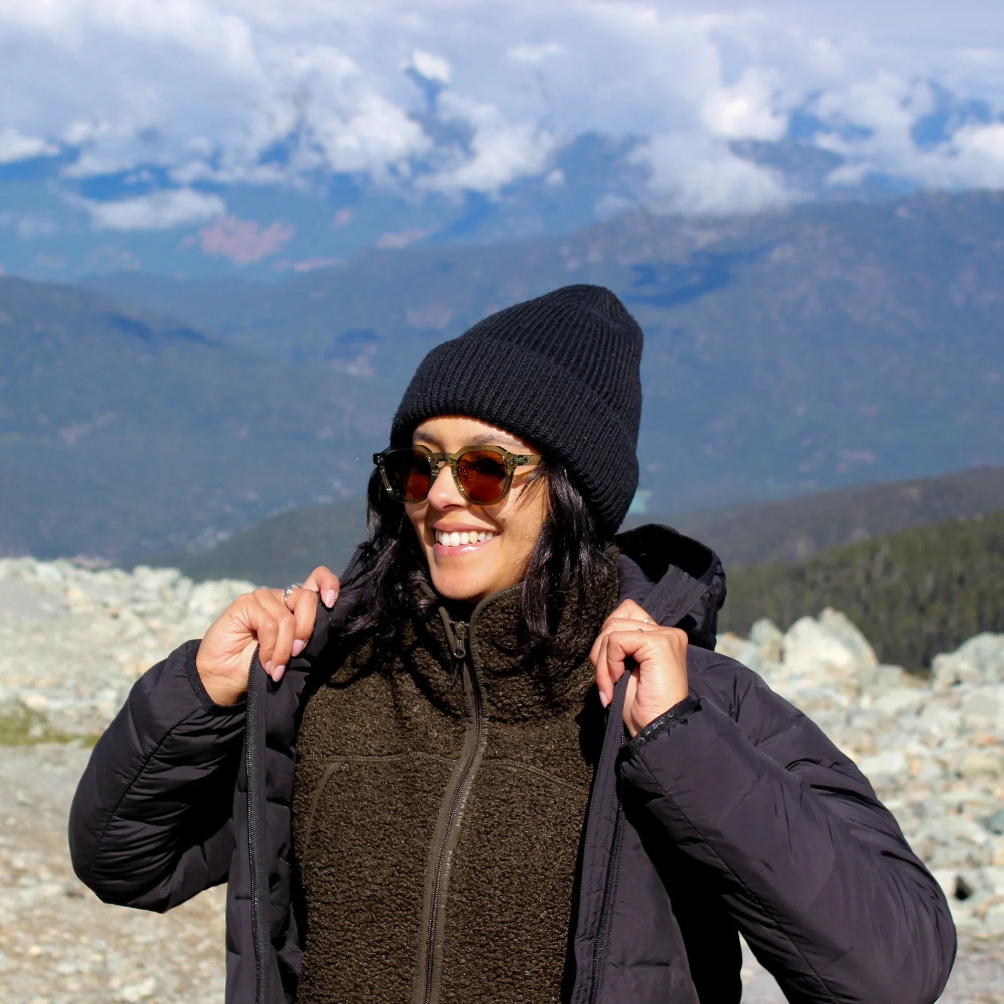 Woman in teddy fleece jacket and beanie smiling outdoors in green mountain landscape