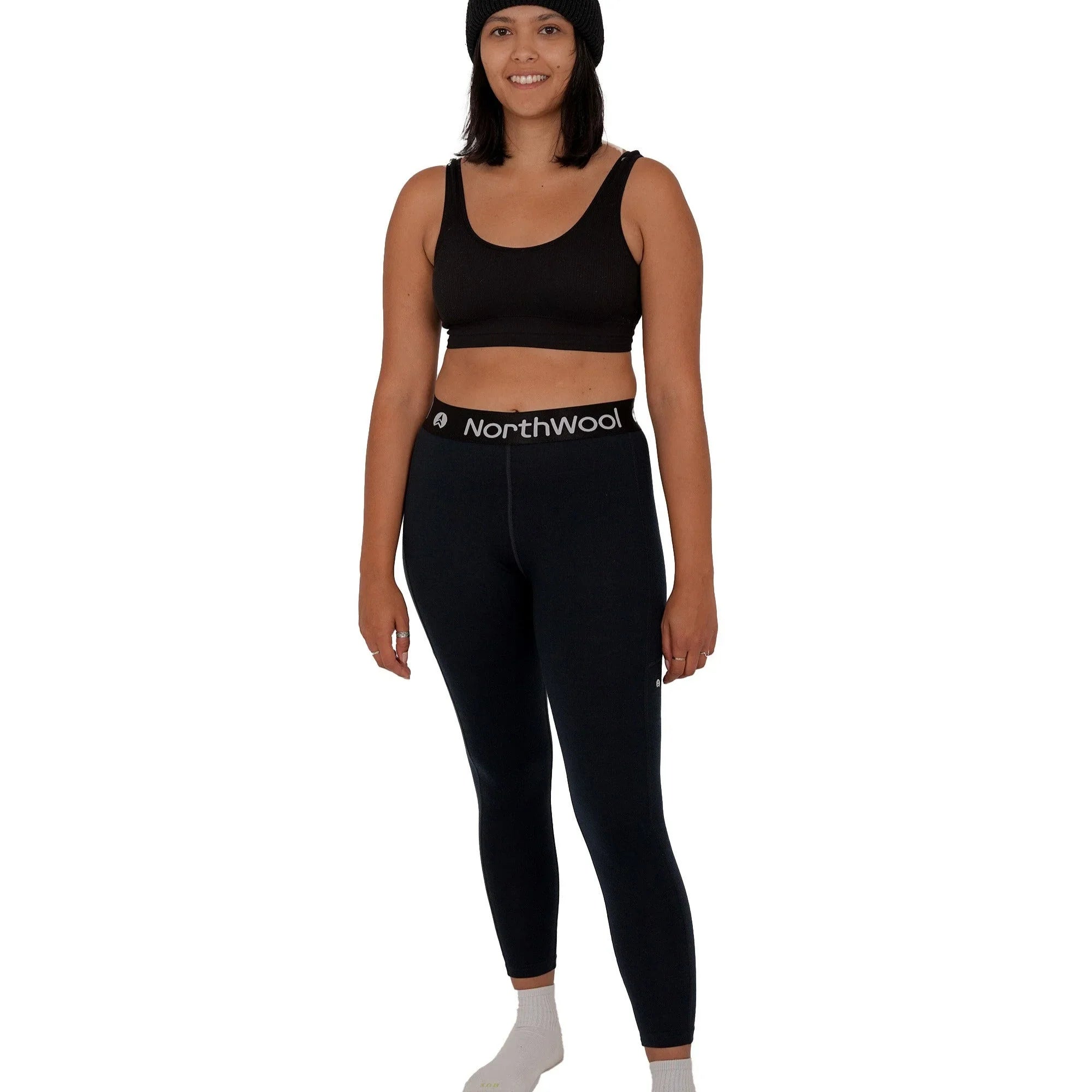 Woman modeling NorthWool black thermal leggings and beanie on white background