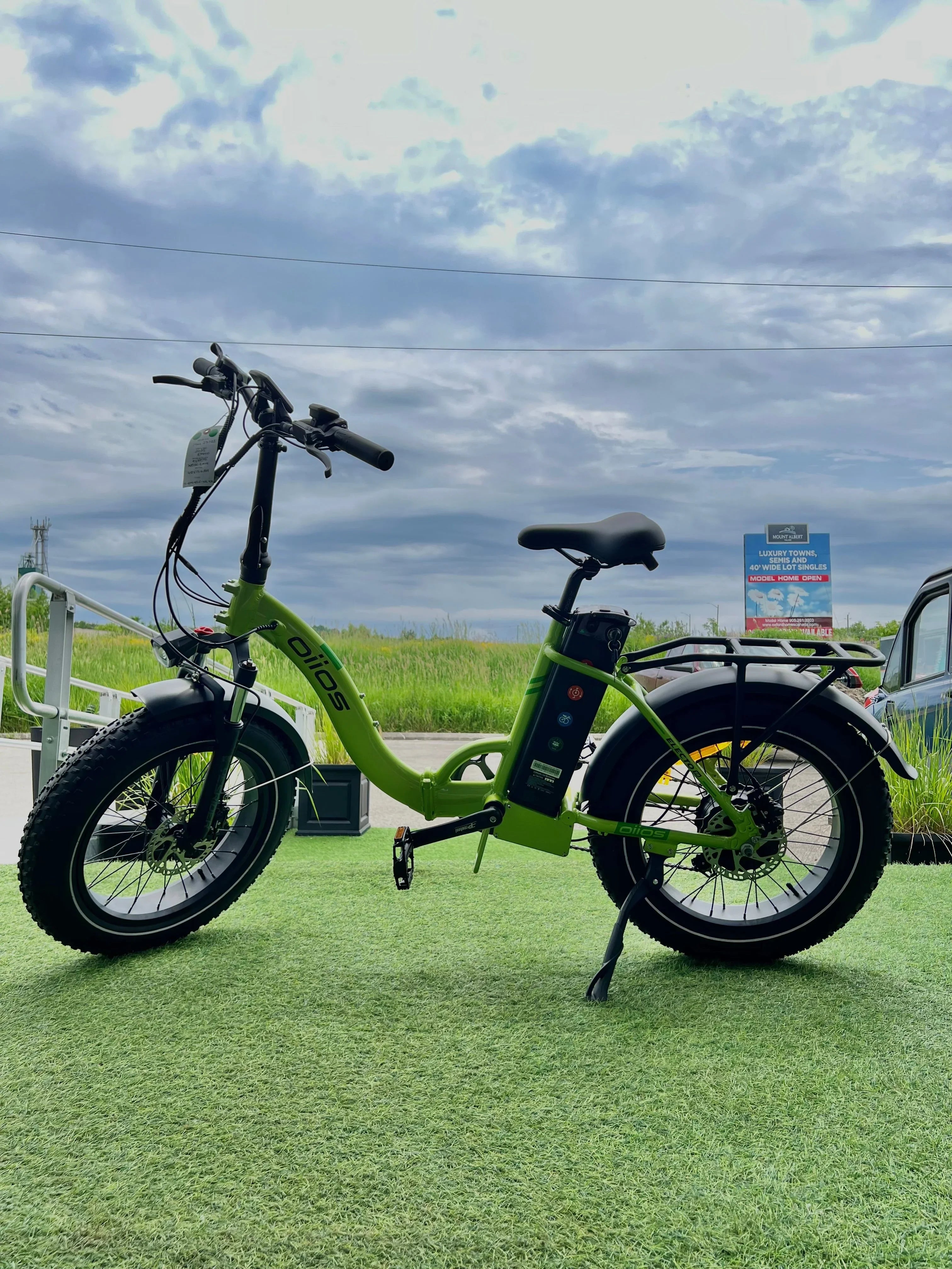 Green OLIOS electric bike with fat tires on artificial grass outdoors under cloudy sky