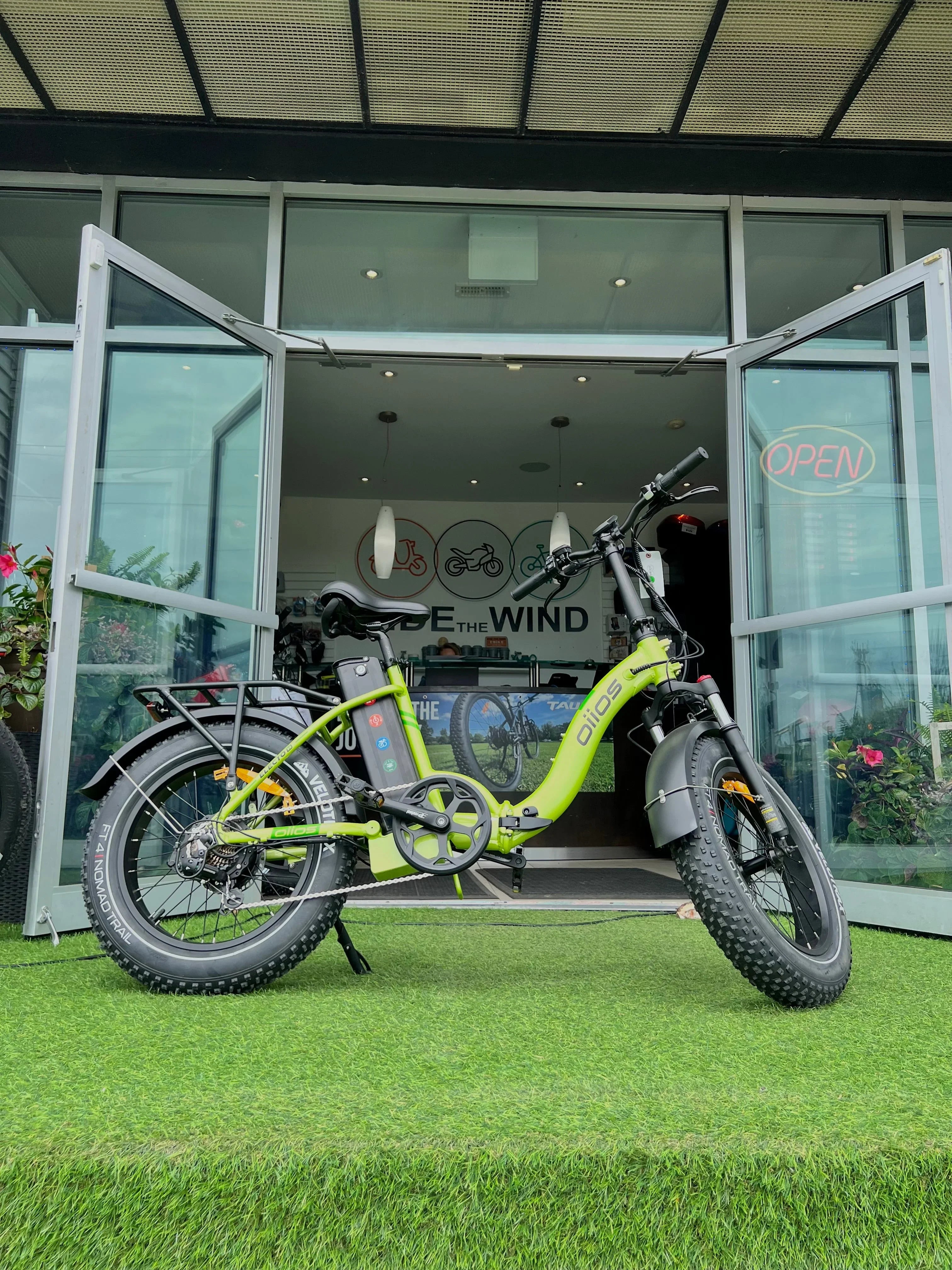 Fat tire electric bike parked on artificial grass outside bike shop with open doors
