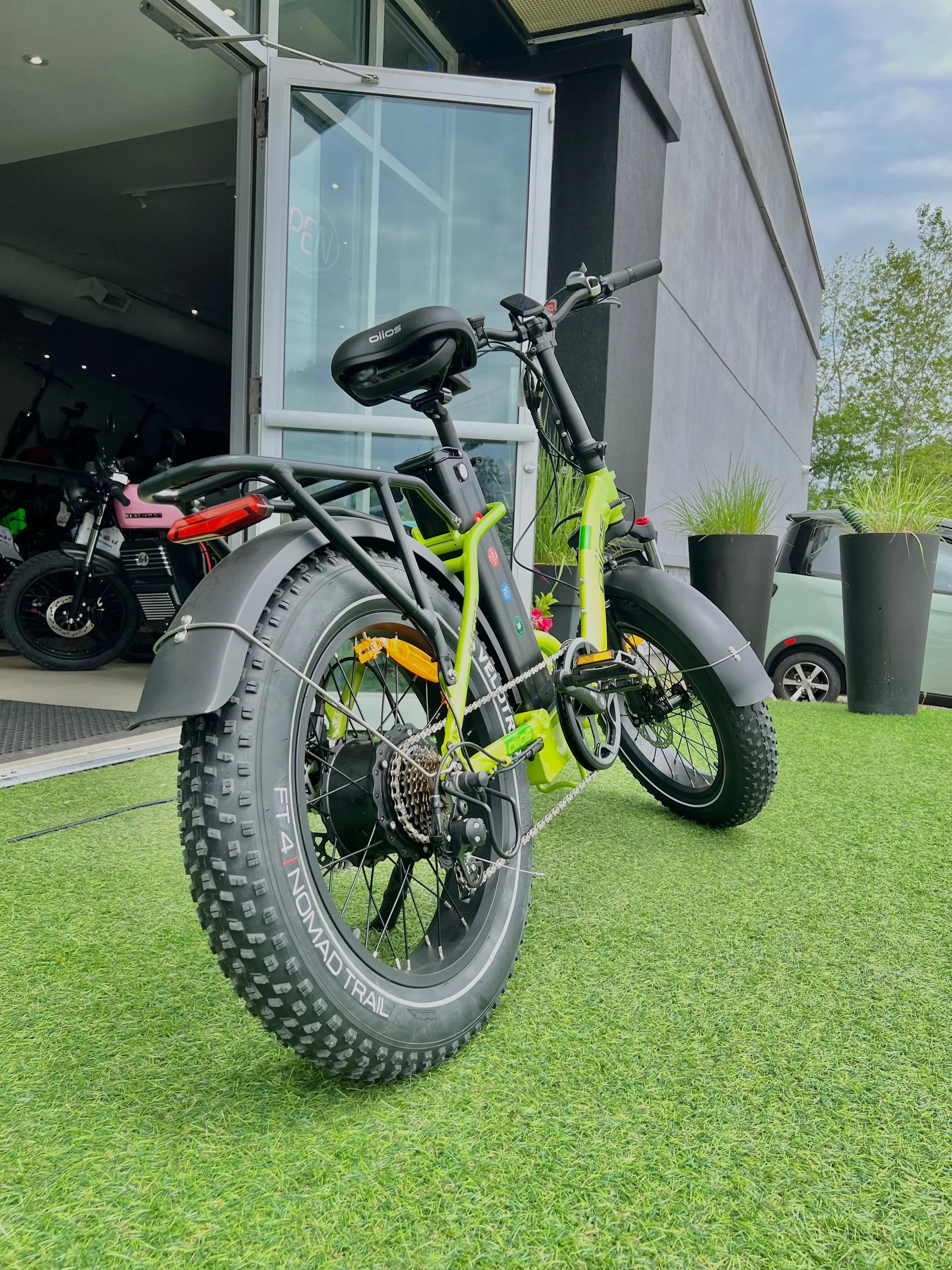 Fat tire electric bike with green frame parked outside shop on artificial grass