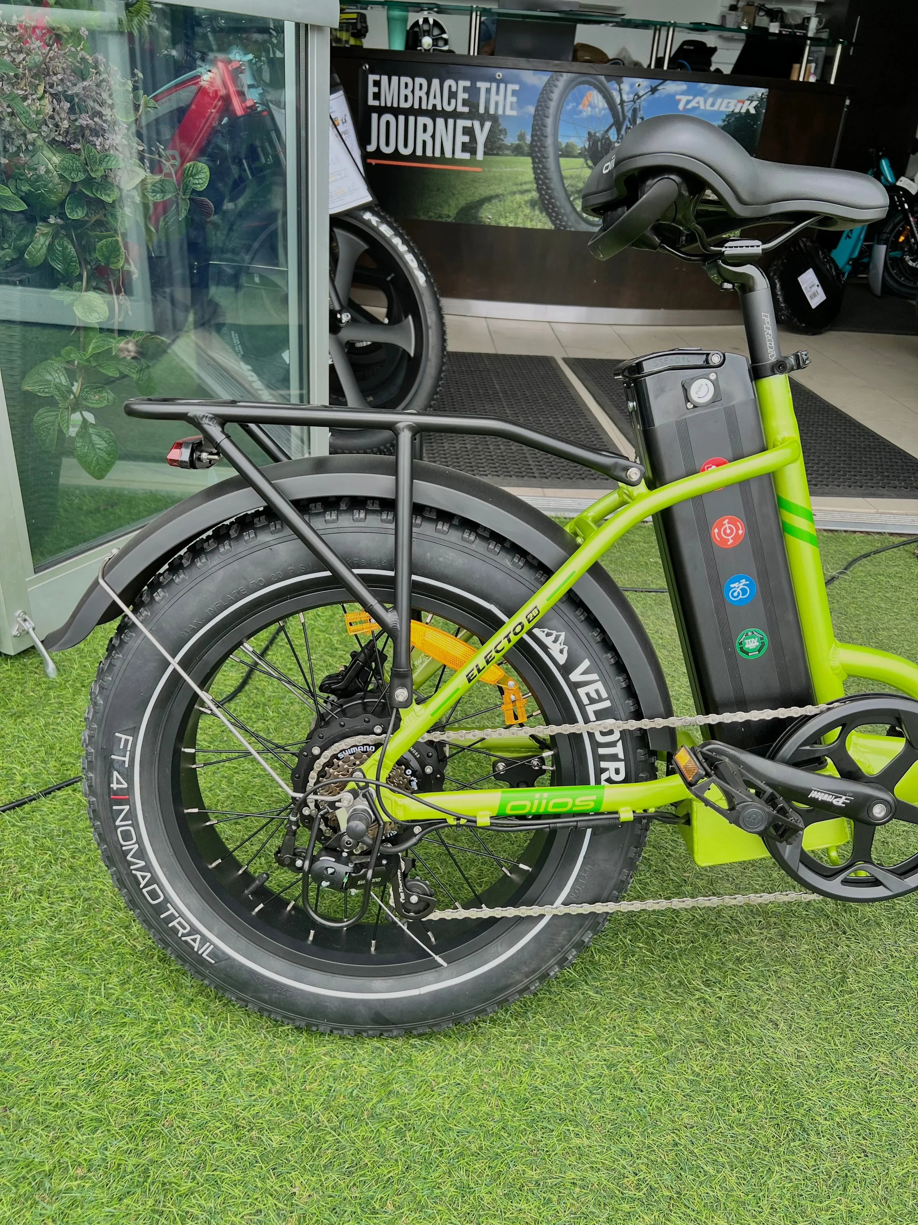 Green electric bike with fat tires on artificial grass, indoor display, 'Embrace the Journey' sign