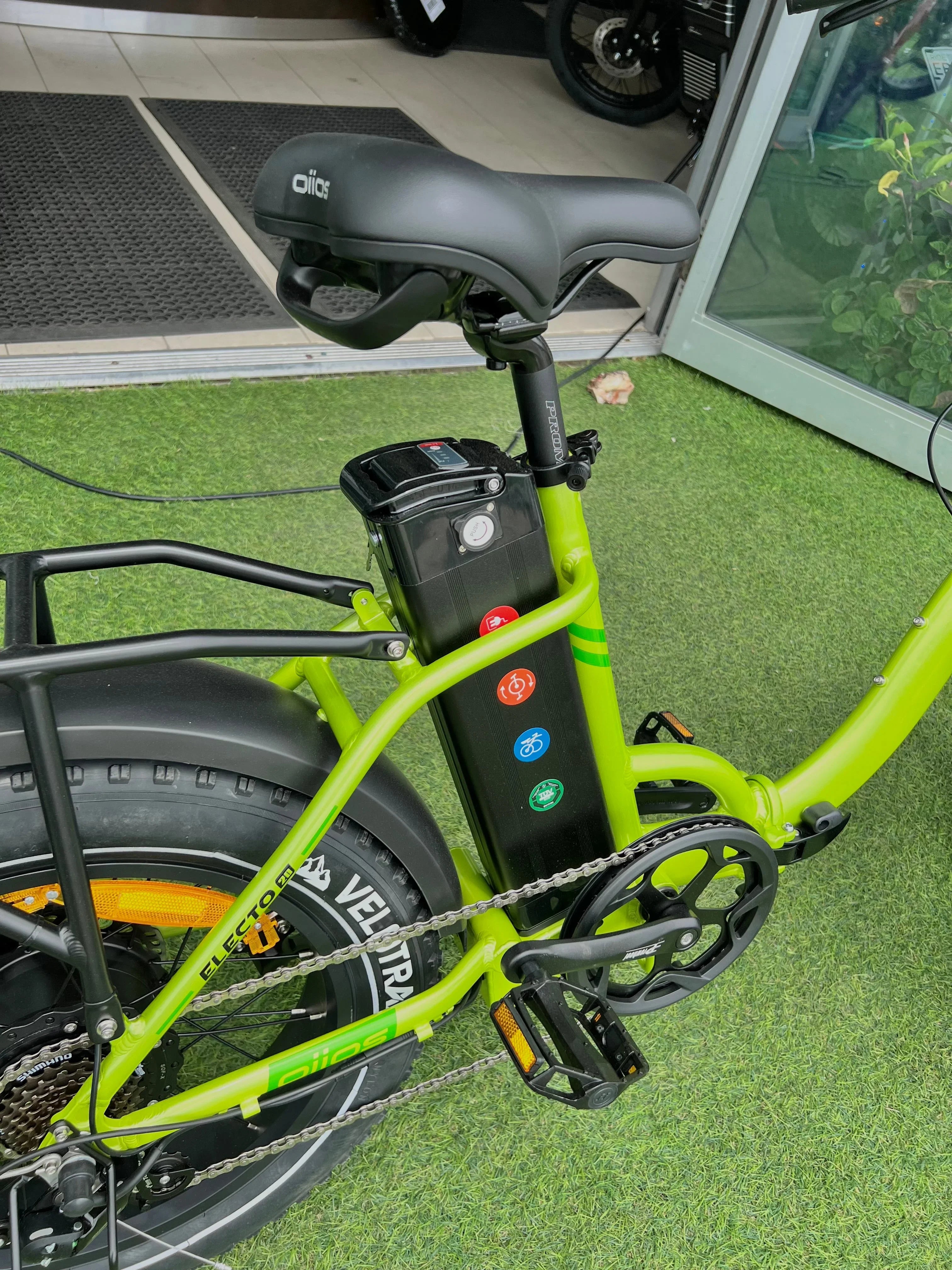 Close-up of a green electric bike frame and battery, black saddle, and Vee Tire rear tire