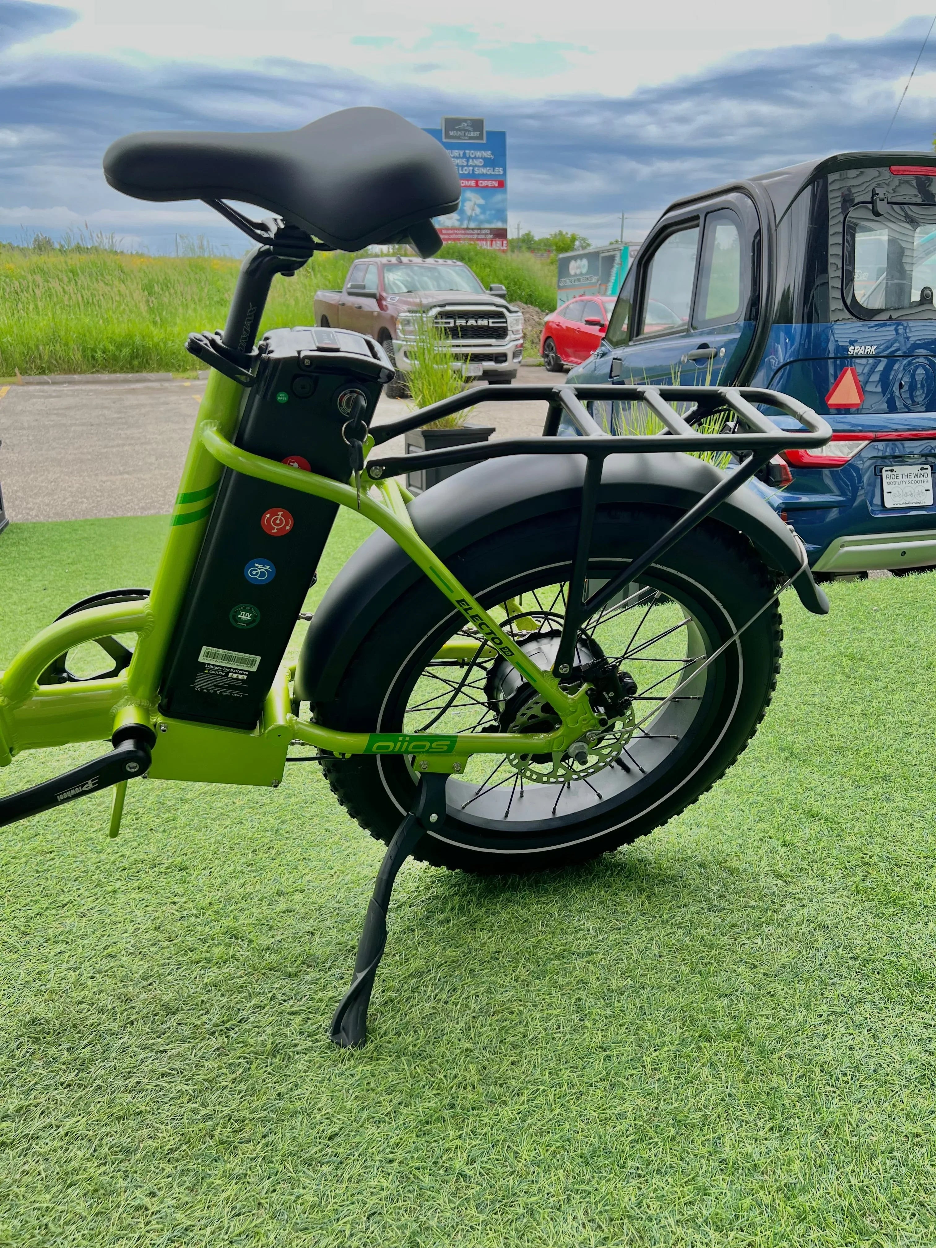 Green electric bike rear wheel and battery on grass, cars in background outdoors