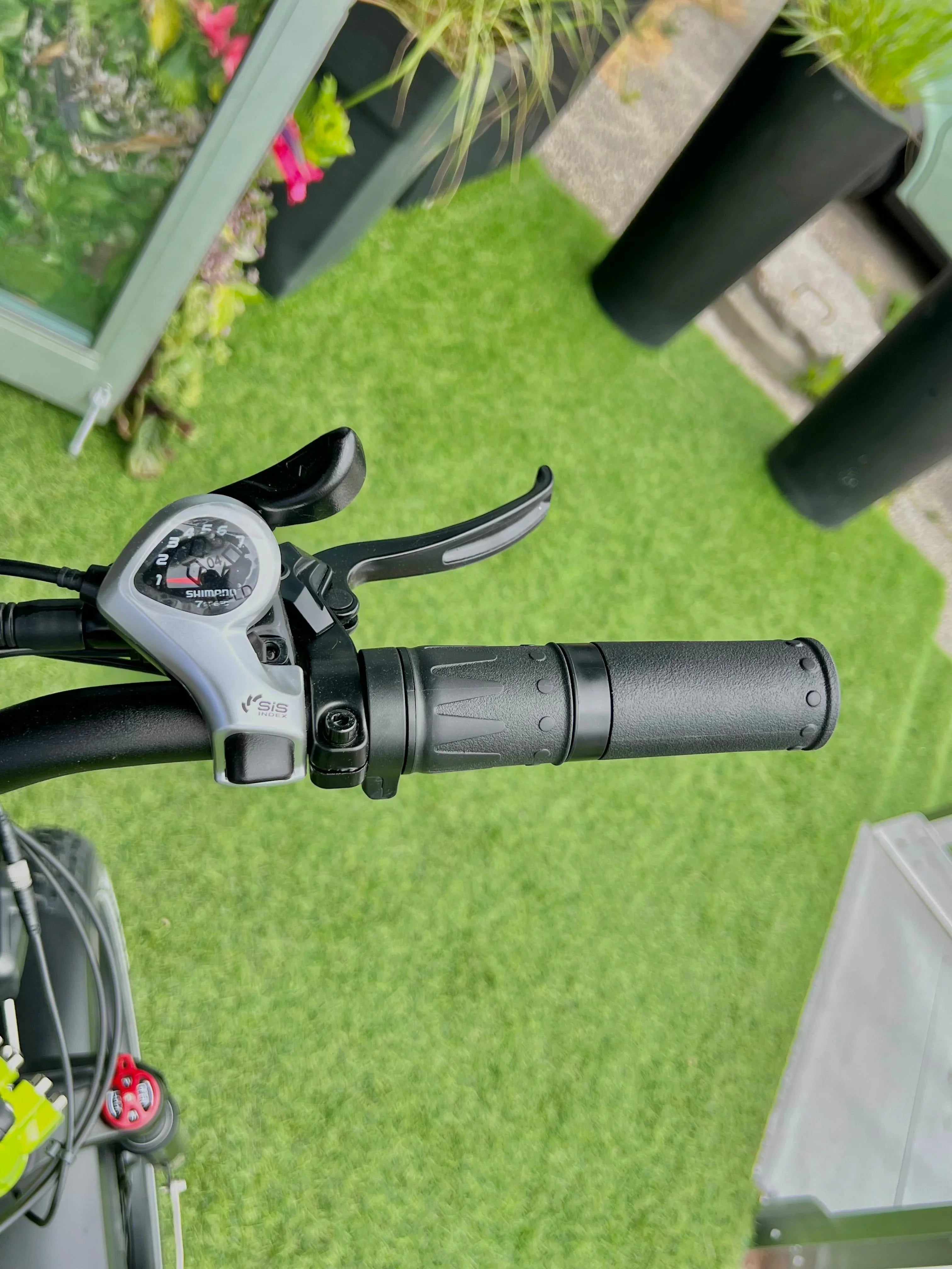 Bicycle handlebar with Shimano gear shifter and black grip on green artificial grass