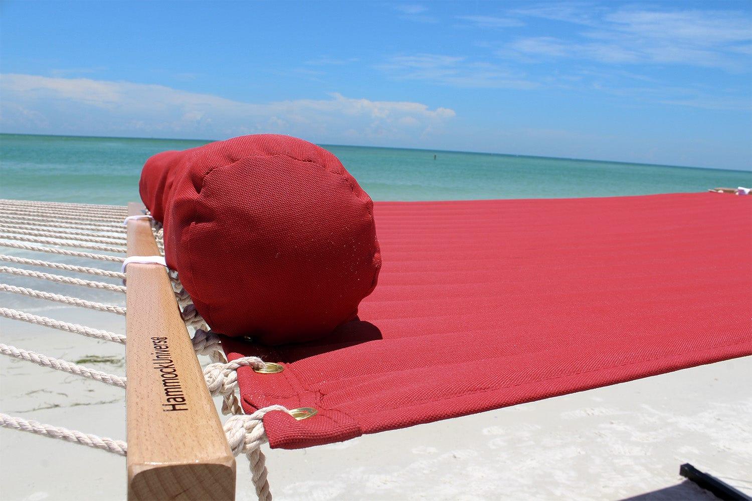 Red olefin fabric double hammock with pillow on sandy beach by the ocean under blue sky