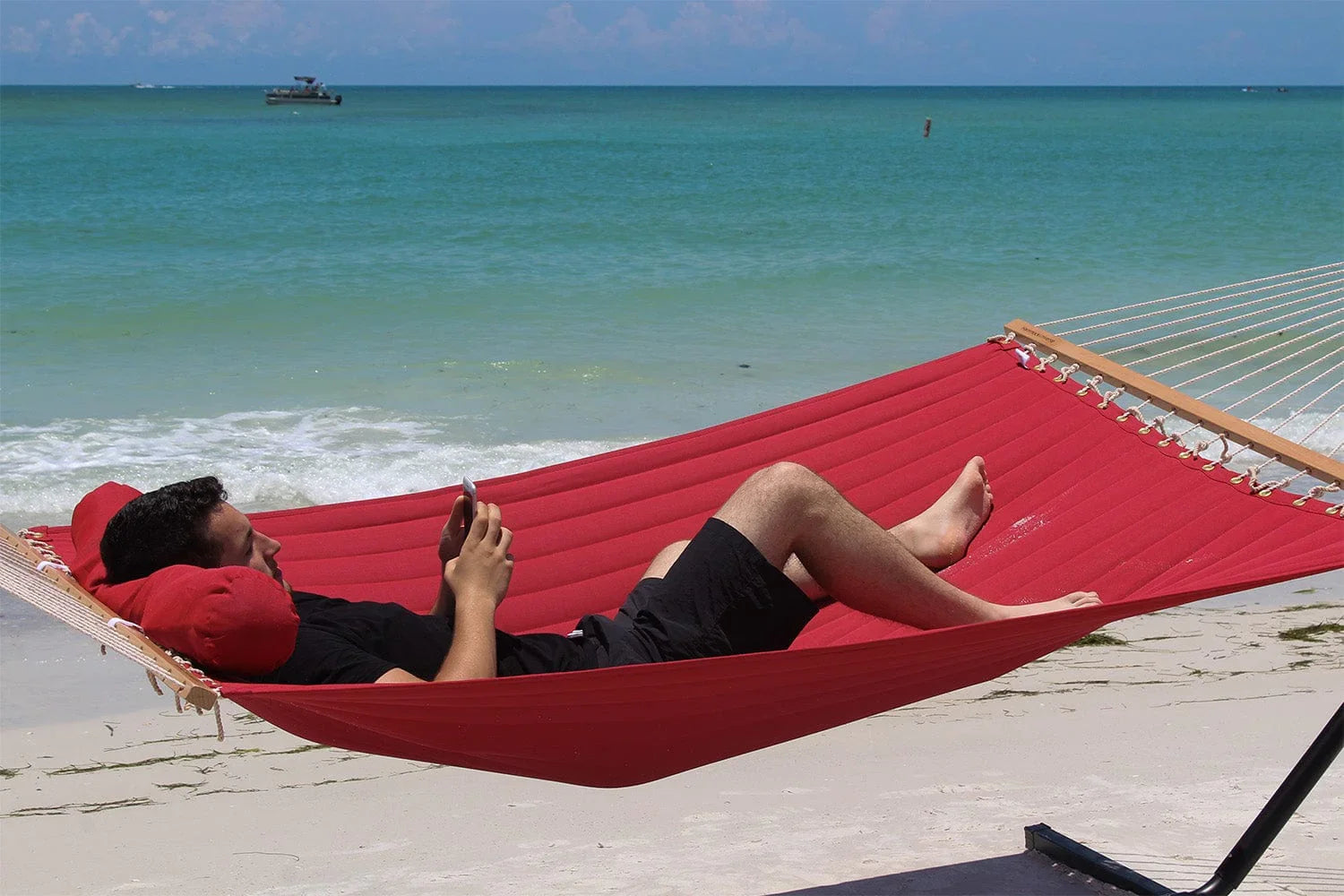 Man relaxing on red olefin hammock by the beach, ocean in background