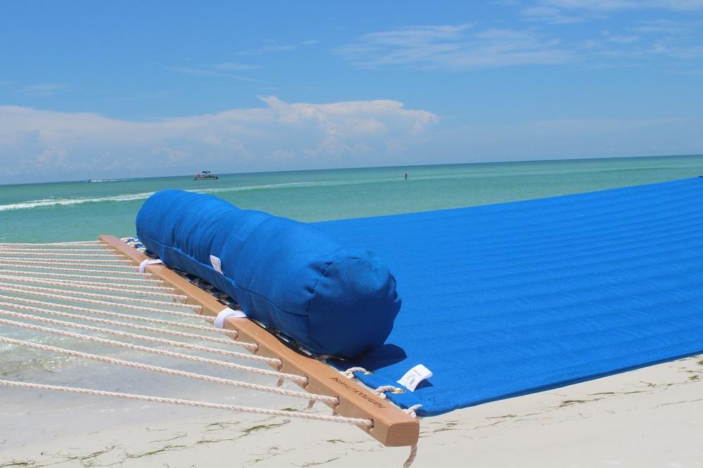 Blue quilted olefin hammock with pillow on a sandy beach by the sea under a clear sky