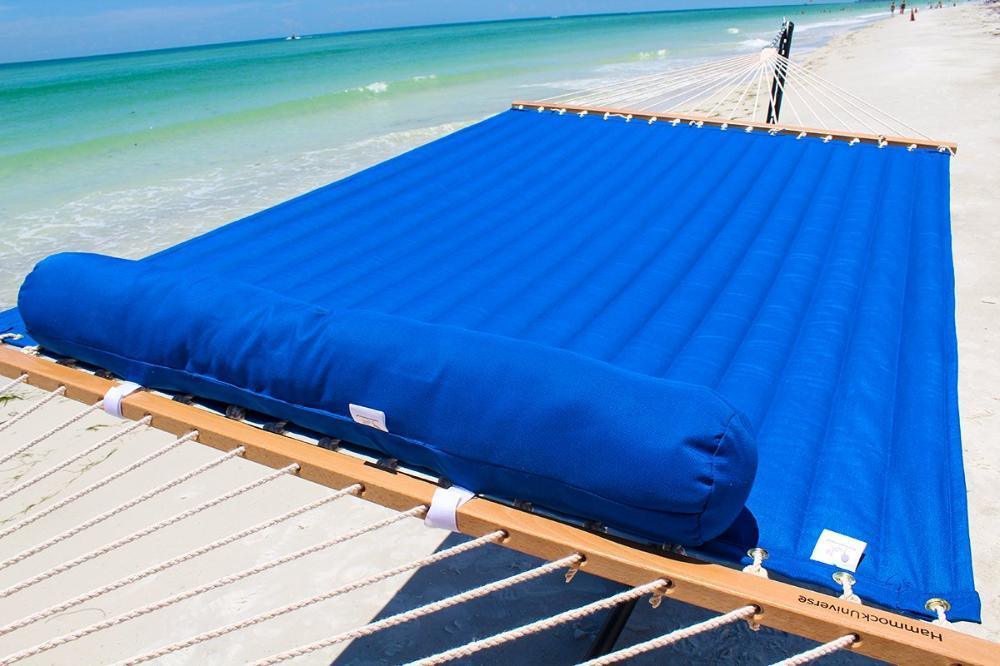 Blue quilted hammock with pillow on sandy beach by ocean, Hammock Universe brand