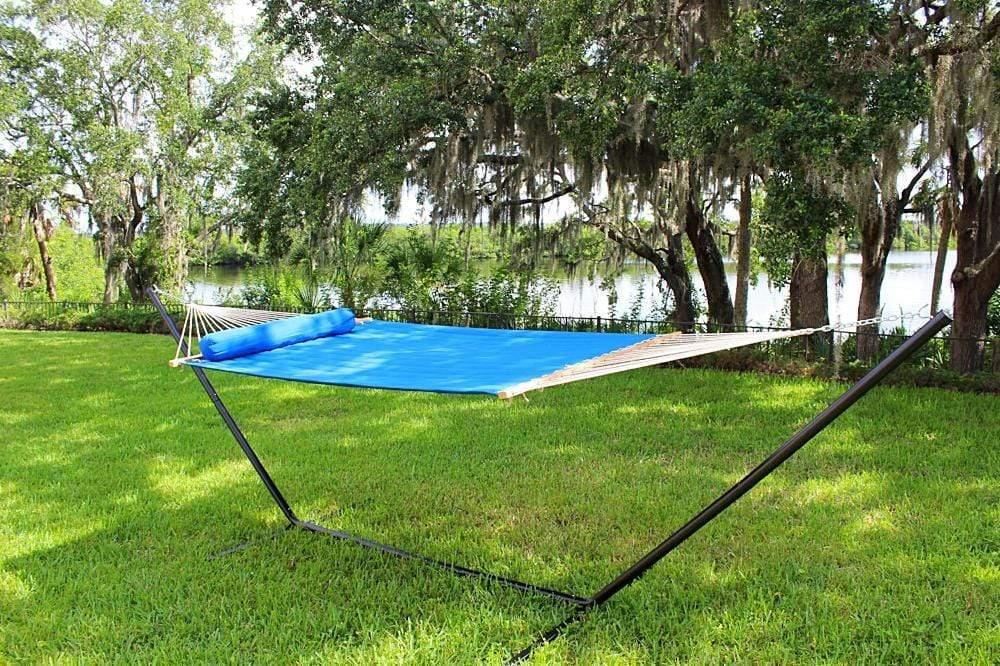 Blue hammock with pillow on metal stand in green backyard by lake and trees
