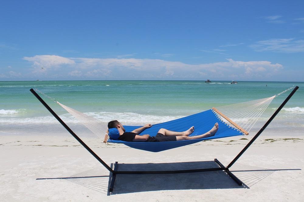 Olefin double quilted blue hammock with tri-beam stand on sandy beach by the ocean