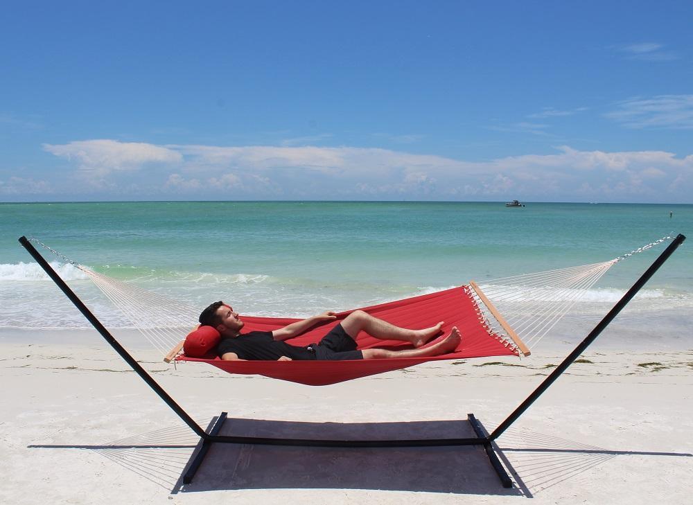 Red olefin double quilted hammock with tri-beam stand on beach by the ocean