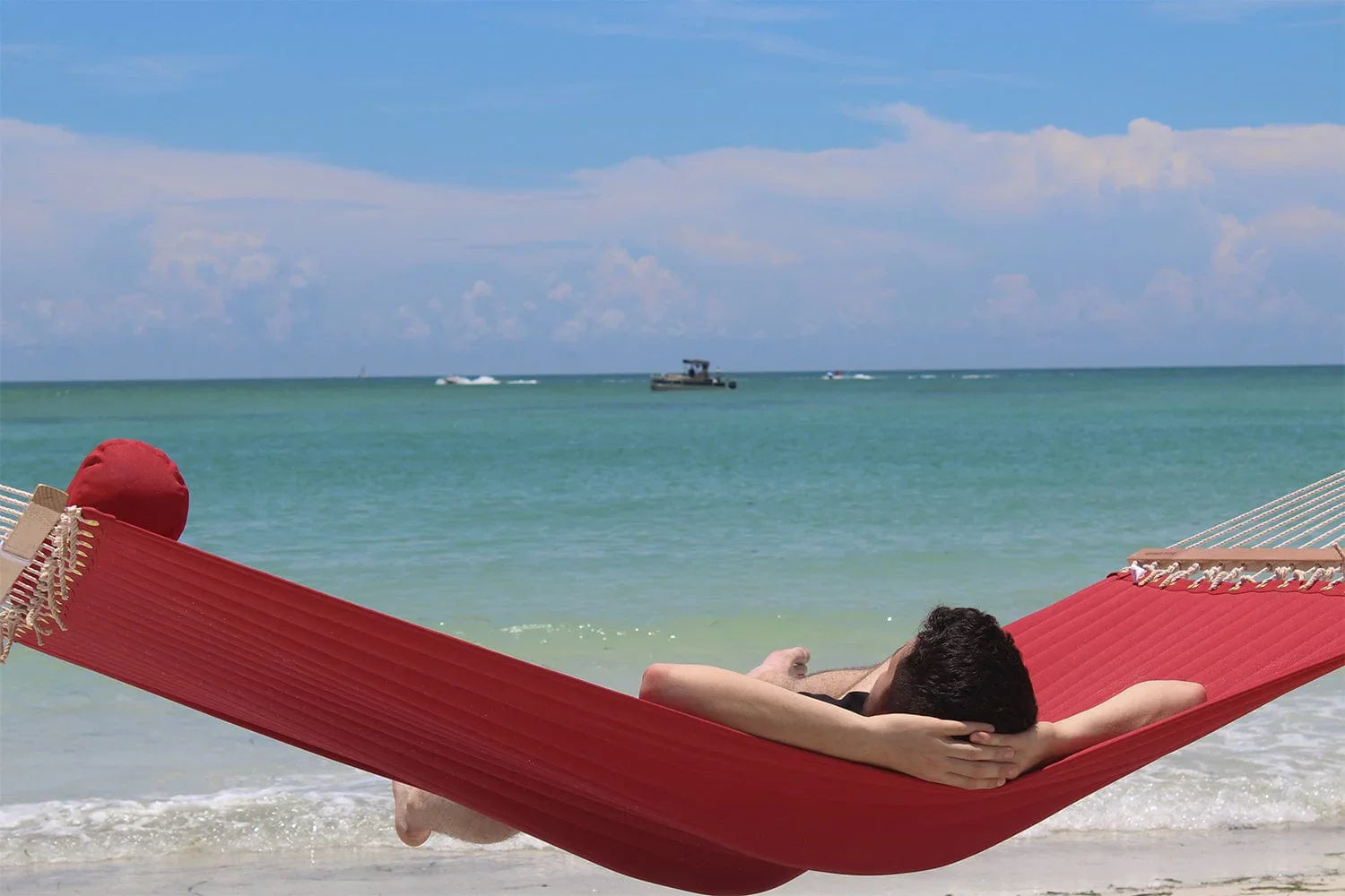 Man relaxing on a red olefin hammock at the beach with blue sea and sky in background