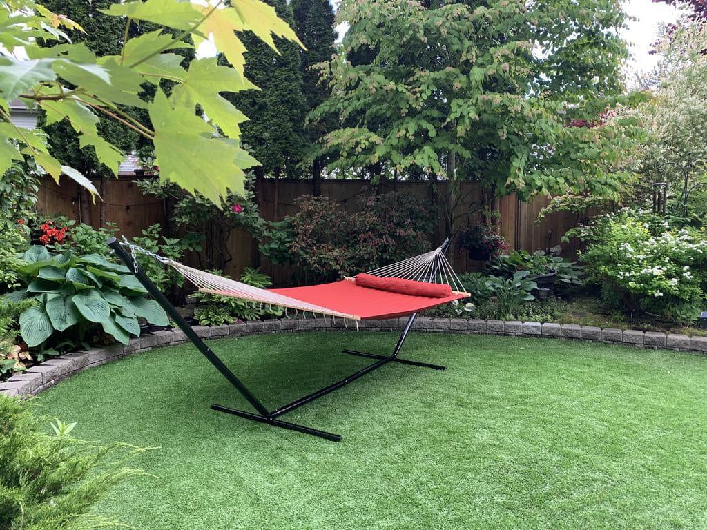 Red double quilted hammock with tri-beam stand in a lush green garden