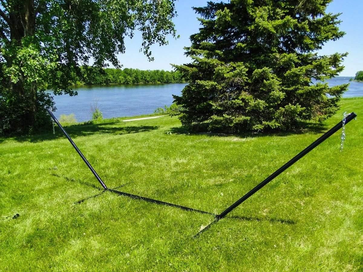 Empty black metal hammock stand on green grass by a lake with trees and blue sky
