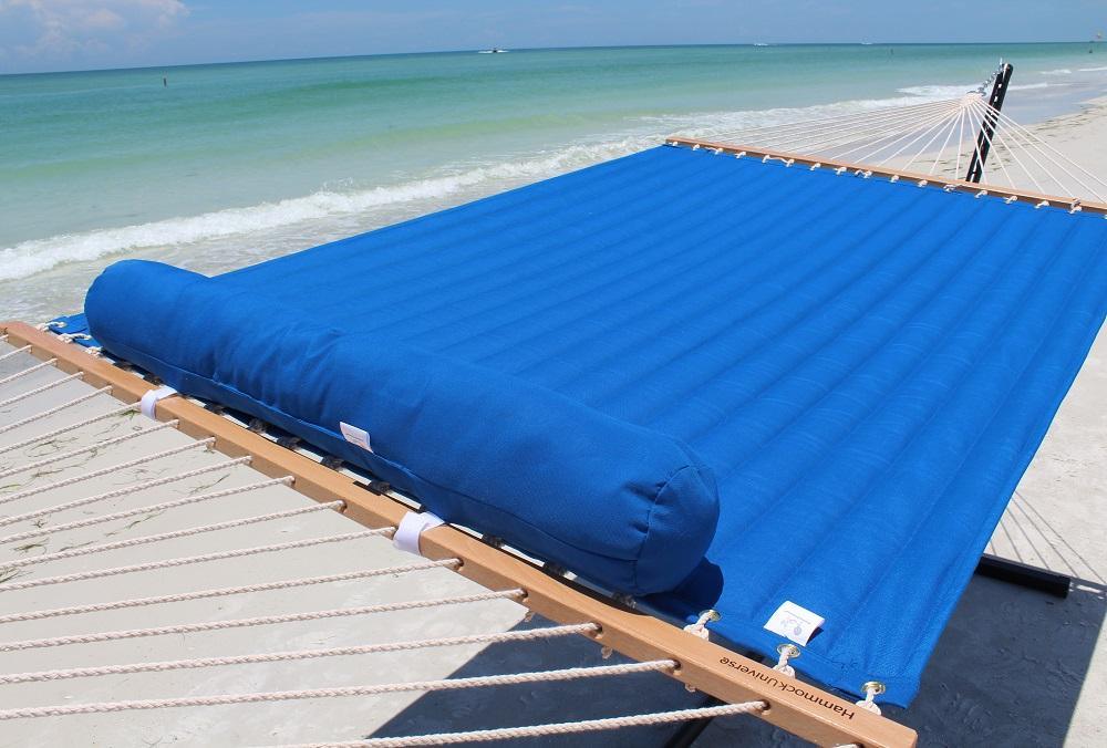 Blue olefin double quilted hammock with pillow on tri-beam stand by the beach