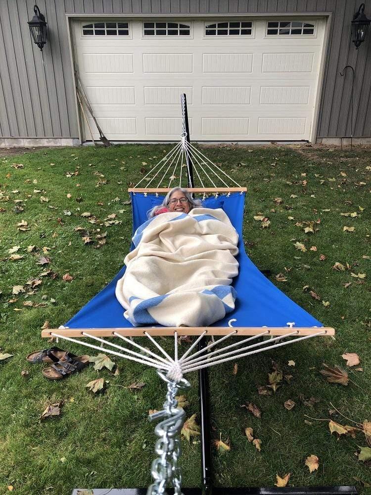 Woman relaxing in a blue olefin single hammock with stand on grass near garage door