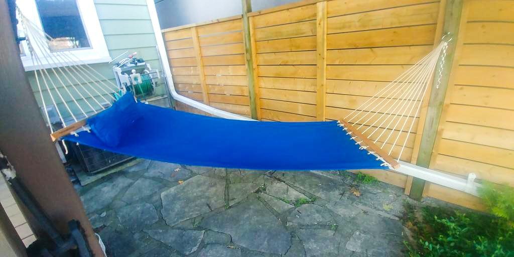 Blue outdoor hammock with wooden spreader bars on stone patio by wooden privacy fence