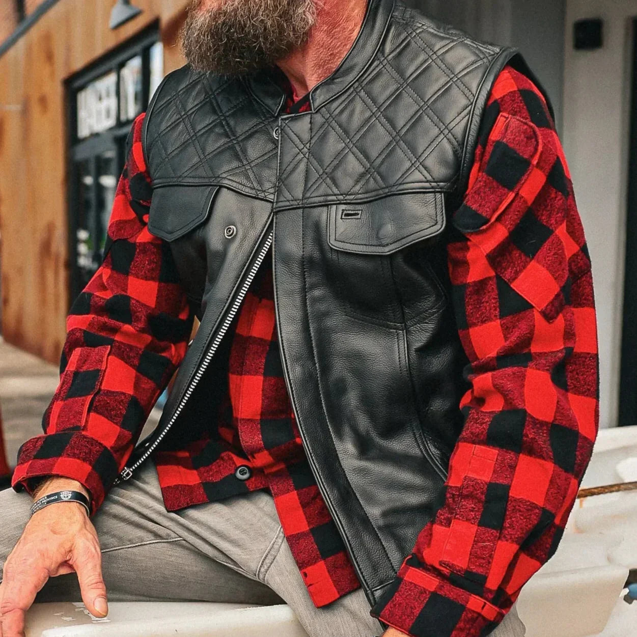 Man wearing black diamond stitch leather club vest over red plaid shirt outdoors