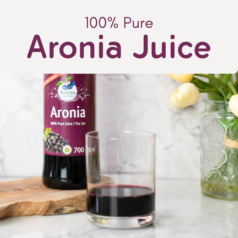 Bottle of 100% pure Aronia juice and glass on marble counter with flowers