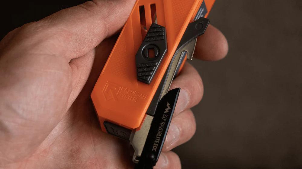 Hand holding orange Drop-Point blade dispenser for razor blade extraction