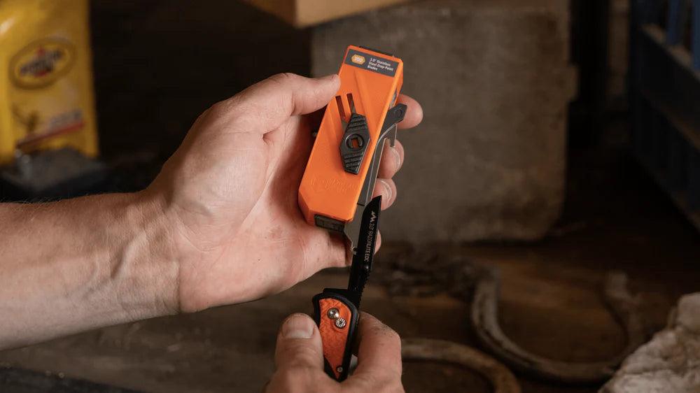 Hand holding orange drop-point blade dispenser and extracting new utility knife blade