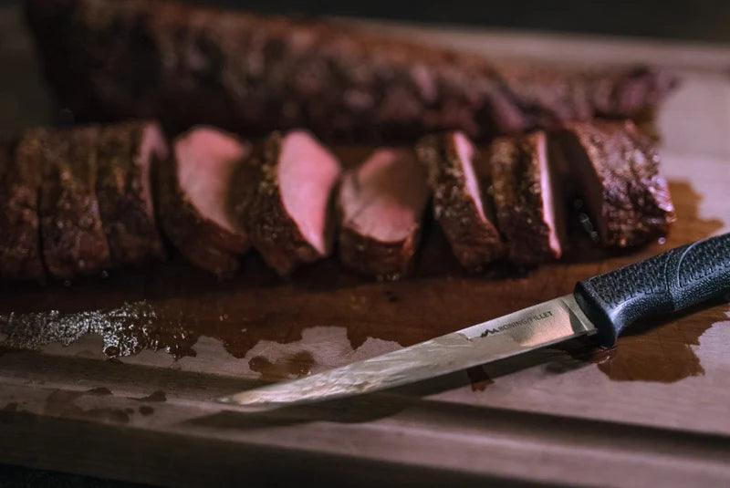 Sliced venison tenderloin on cutting board with boning knife, game meat preparation