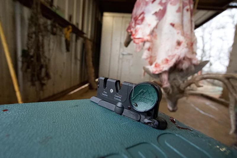 GamePro Sharpener on green case in garage with deer carcass hanging in background