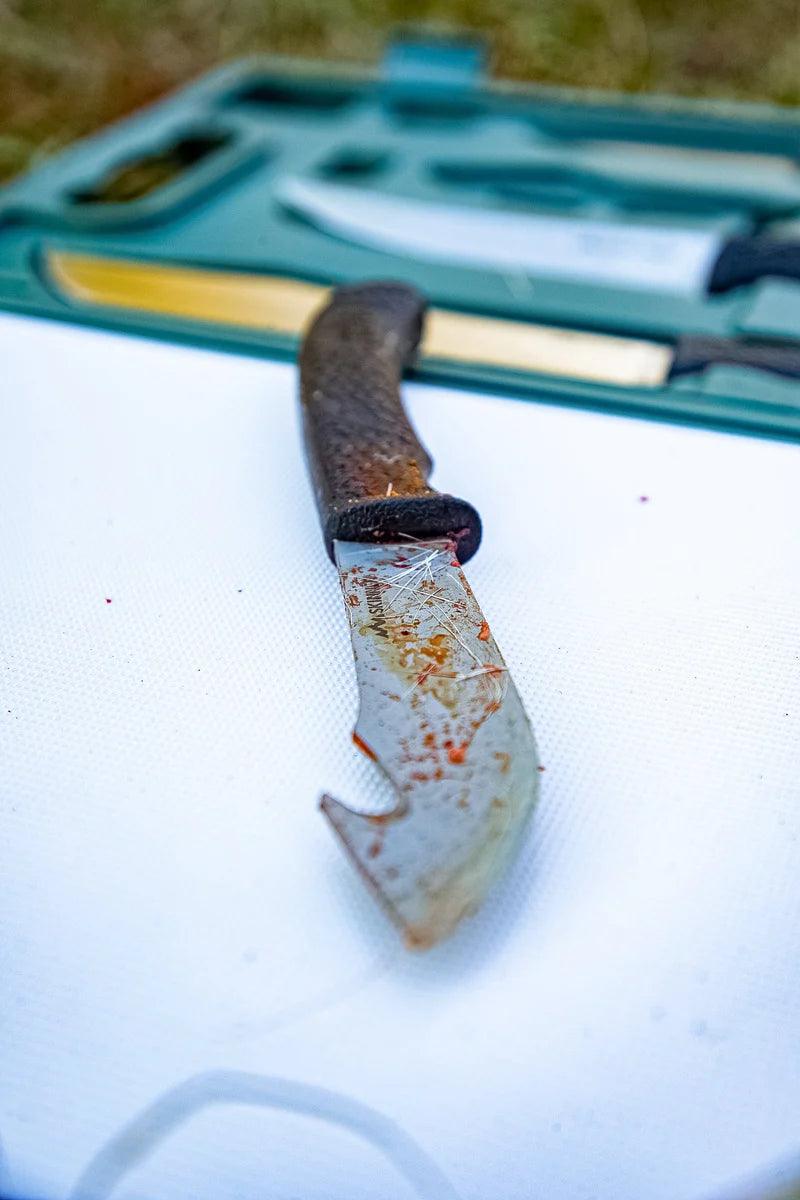 GamePro Skinner hunting knife with textured handle and stained blade on white cutting board