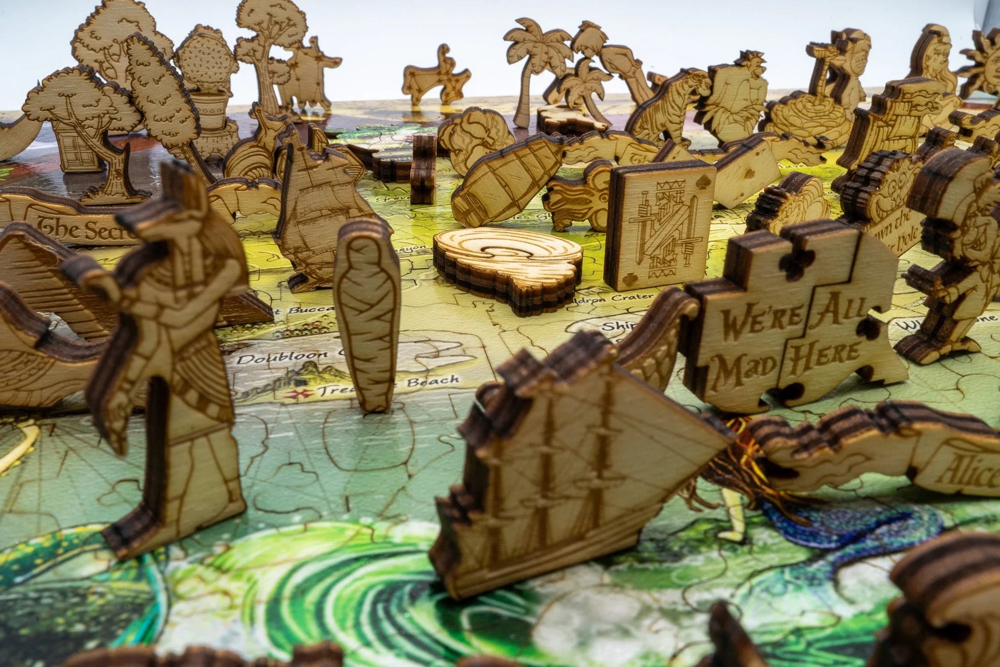 Laser-cut wooden puzzle pieces shaped like ships, trees, and characters on a fantasy board game map