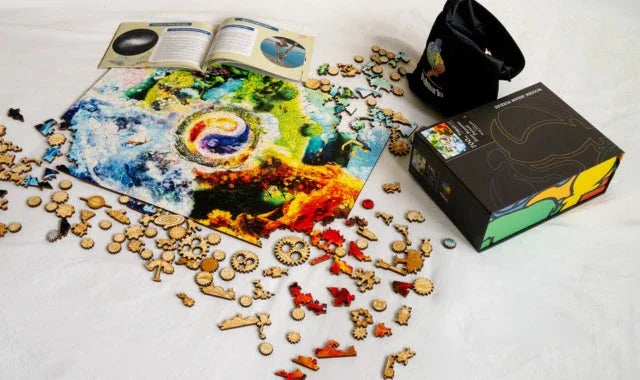 Colorful wooden puzzle pieces, vibrant art print, black box, and open booklet on white surface