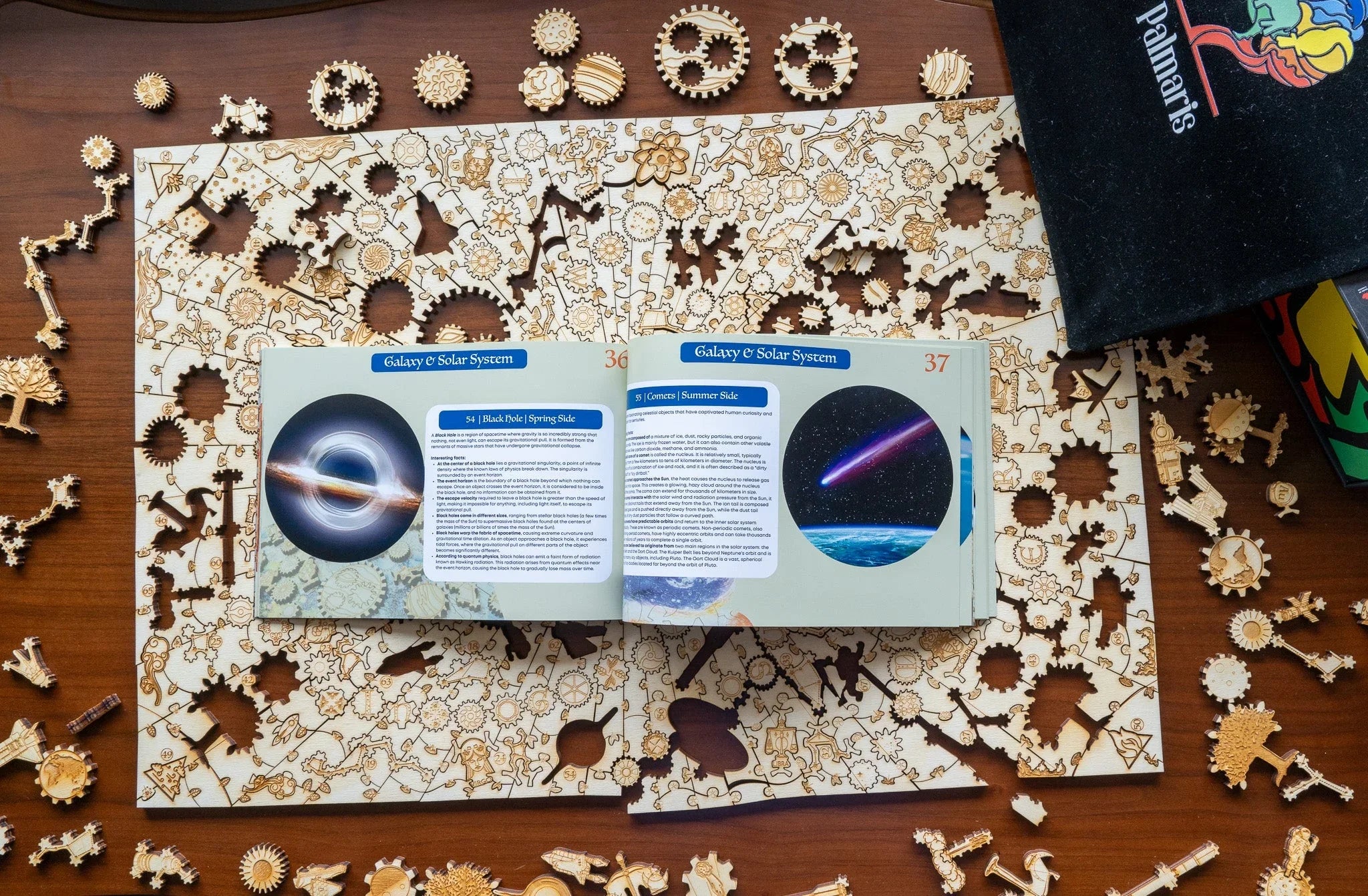 Wooden galaxy solar system puzzle with gears and open astronomy book on brown table