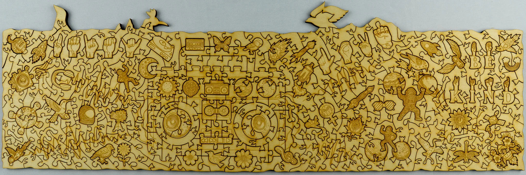 Laser-cut wooden puzzle with engraved nature and peace symbols, text 'BE KIND,' birds, astronaut.