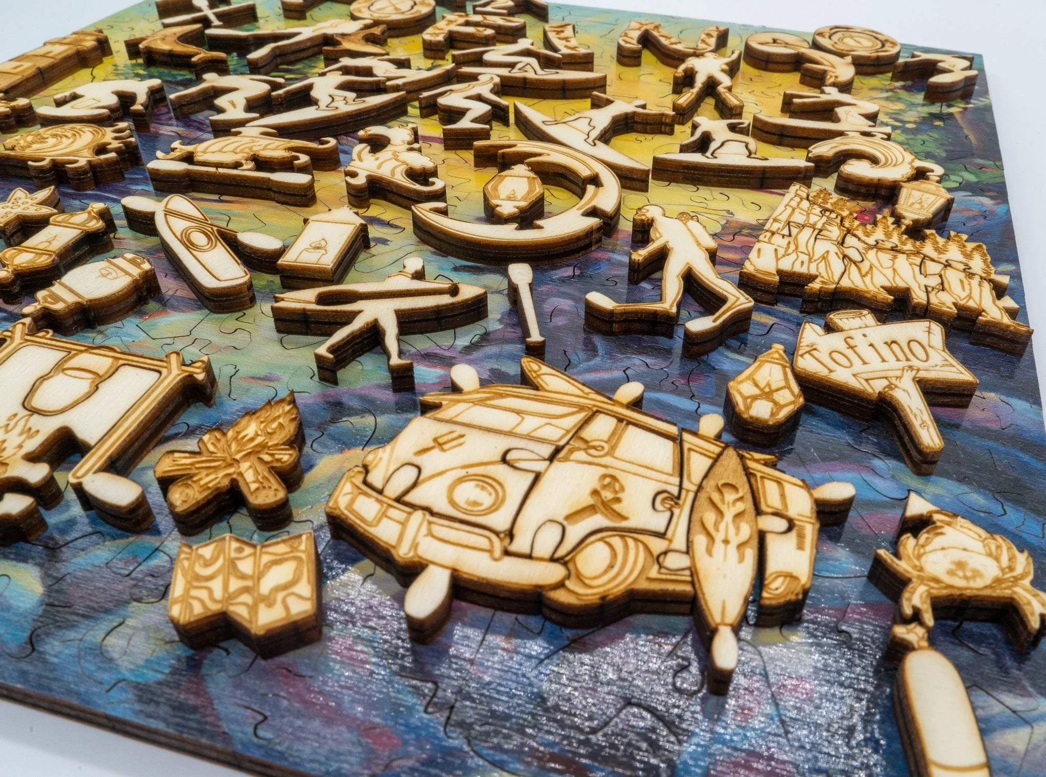 Laser-cut wooden puzzle pieces with Tofino symbols, camper van, maps, and outdoors theme.
