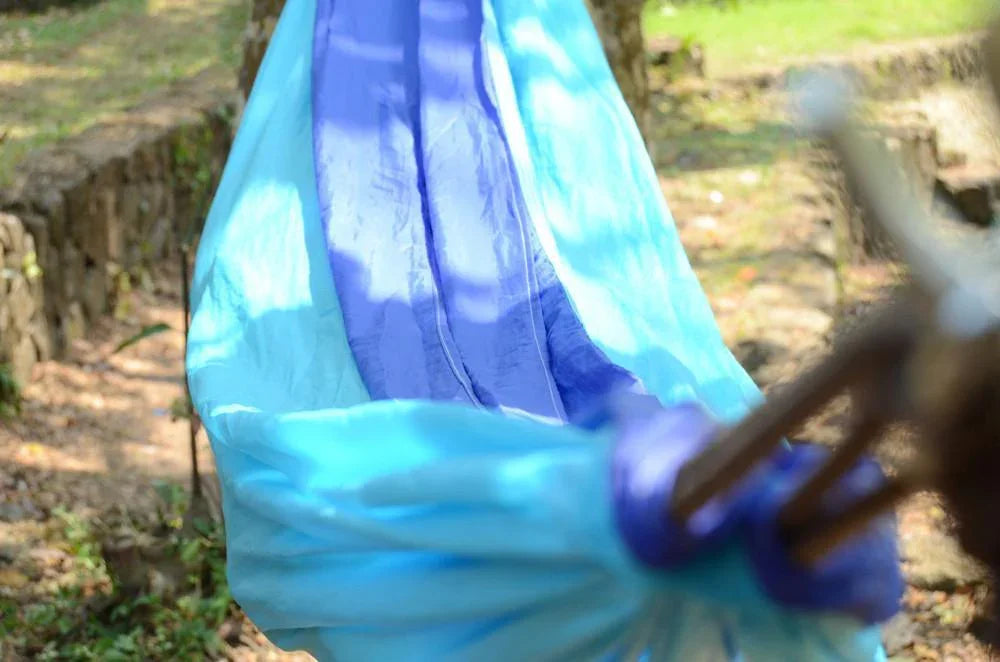 Blue and turquoise nylon hammock tied outdoors in a sunny garden setting