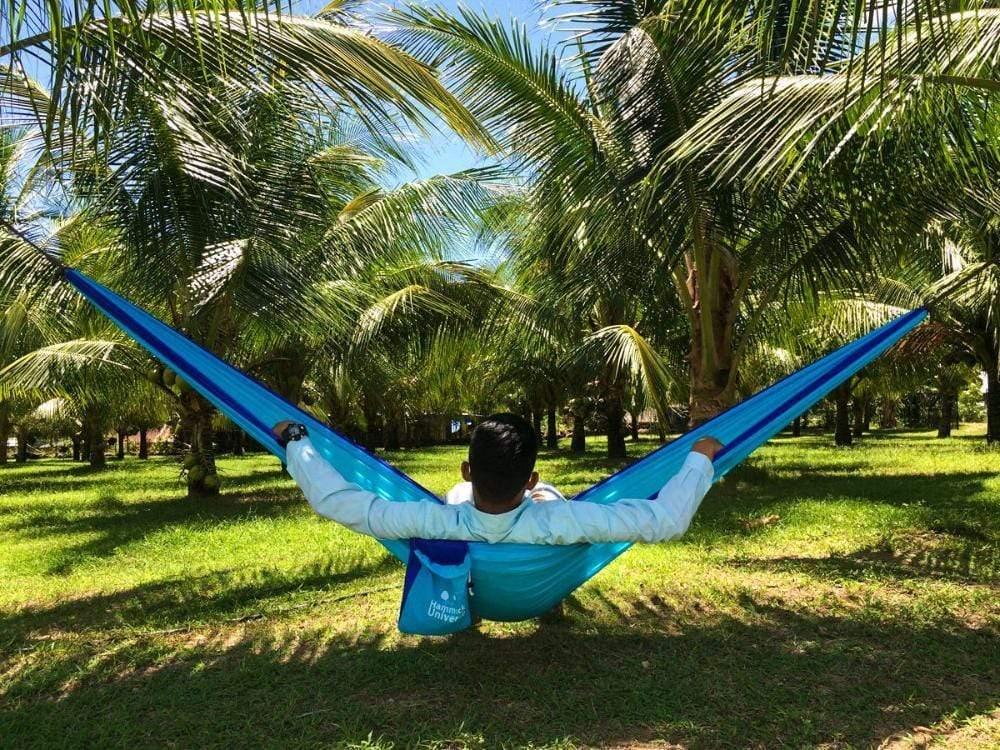 Man relaxing in a blue double parachute hammock under palm trees outdoors