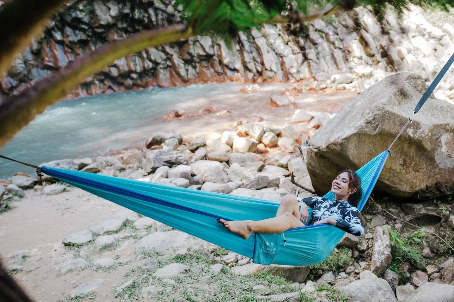 Woman relaxing in a blue hammock by a rocky river outdoors