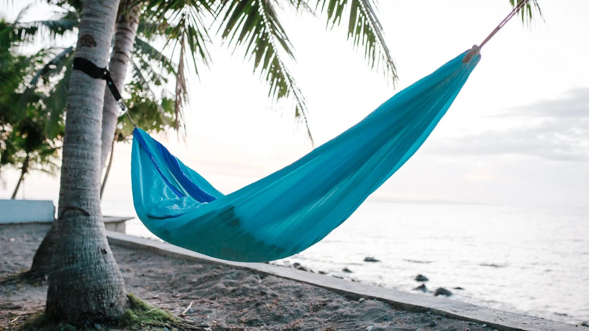 Blue hammock tied to palm trees on tropical beach at sunset