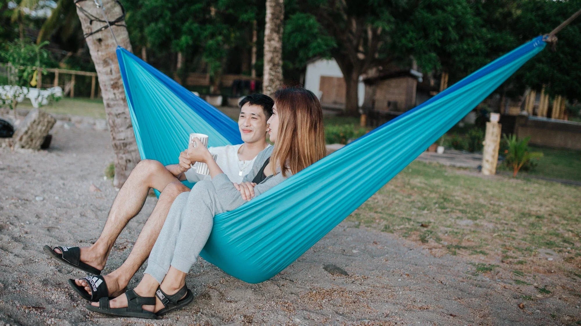 Couple relaxing in a turquoise hammock on a sandy outdoor area with trees
