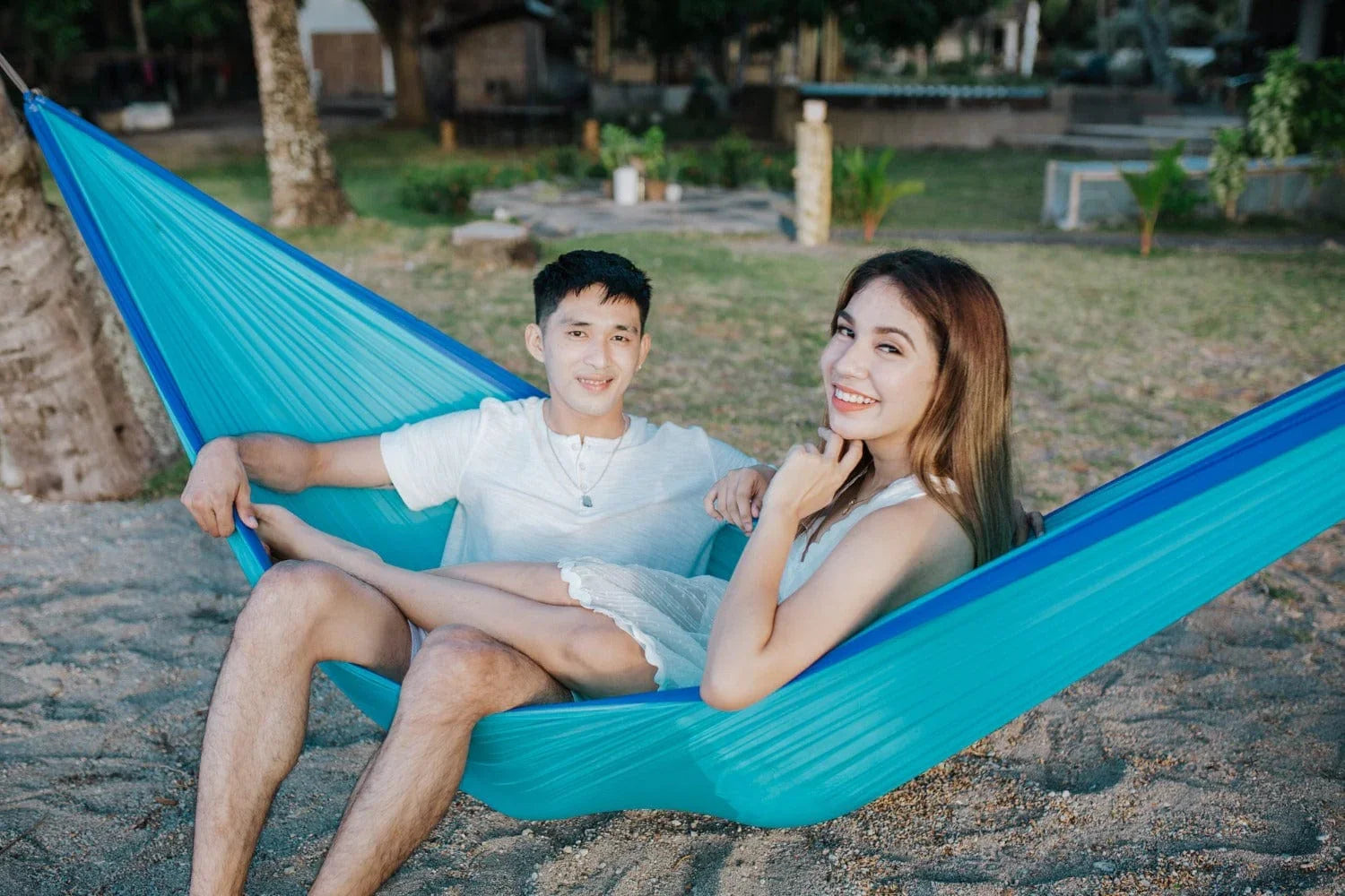 Smiling couple relaxing in a blue hammock on a sandy beach resort