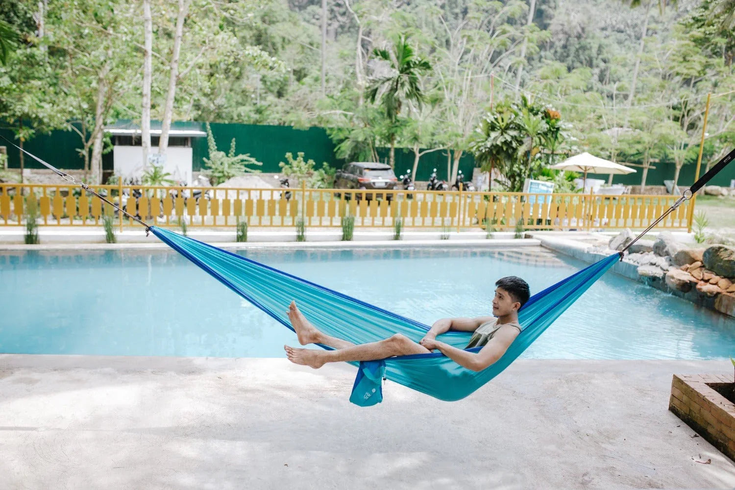 Man relaxing in a blue hammock by a poolside in a tropical outdoor setting